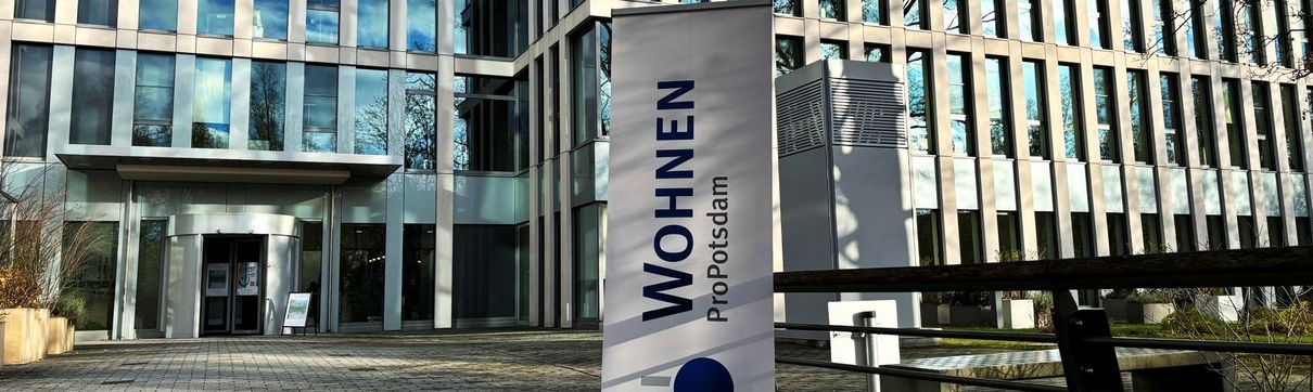 Vor einem großen Gebäude mit vielen Fenstern steht ein Banner mit der Aufschrift ProPotsdam Wohnen.