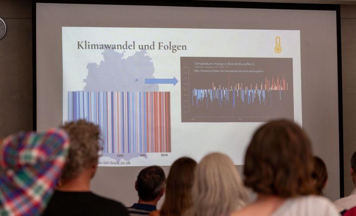 Grafik auf Beamer-Leinwand, vor der viele Menschen sitzen