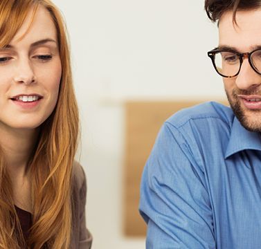 Eine Frau und ein Mann schauen gemeinsam mit einer Beraterin auf etwas auf einem Tisch