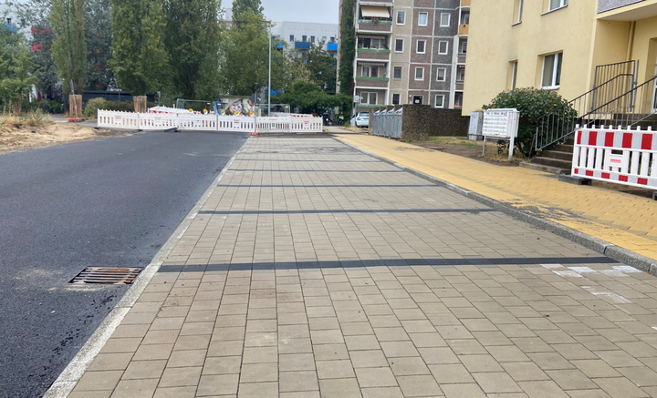 Neu gepflasterte Straße und Parklätze neben einem gelben Wohngebäude.