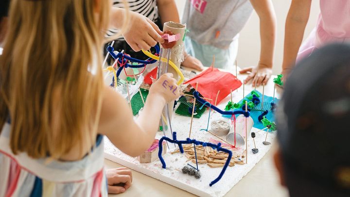 Kinder, die um einen Tisch herum stehen, bauen aus einfachen Bastelmaterialien einen Spielplatz