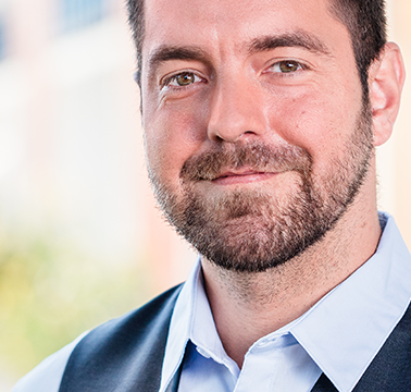 Freundlicher Wohnservice-Mitarbeiter, der vor einem Haus stehend bei sonnigem Wetter in die Kamera blickt