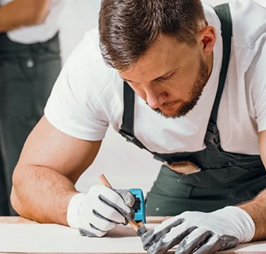 Ein Schreiner markiert auf einer Holzlatte eine Stelle für das Sägen mit einer Stichsäge