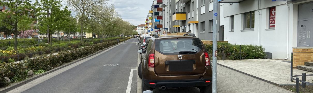 Straßenfluchtansicht mit parkenden Autos auf dem linken Parkstreifen.