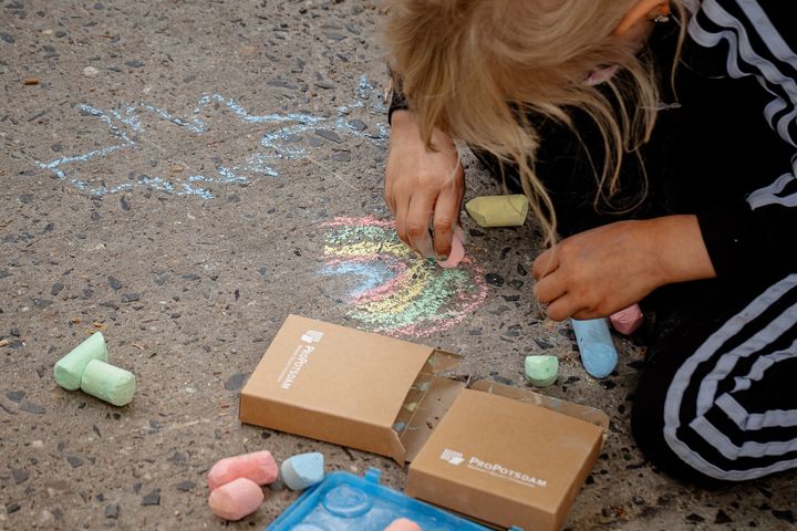 Kind hockt auf Straße und malt diese mit bunter Kreide an