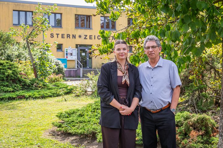 Frau und Mann stehen im grünen Garten vor einem gelben, zweietagigen Haus