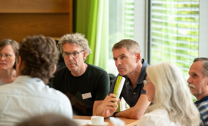 Menschen sitzen am runden Tisch und diskutieren miteinander