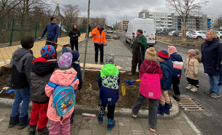 Mehrere Kinder die am Straßenrand einen Baum einpflanzen.