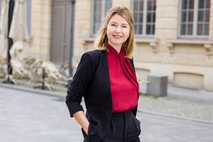 Blonde Frau mit roter Bluse und schwarzem Blaser.