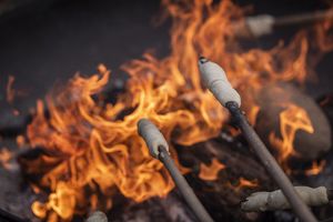 Zwei Stöcke mit Marshmallows an den Enden werden über einem Lagerfreuer gehalten