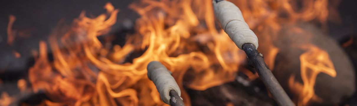 Zwei Stöcke mit Marshmallows an den Enden werden über einem Lagerfreuer gehalten