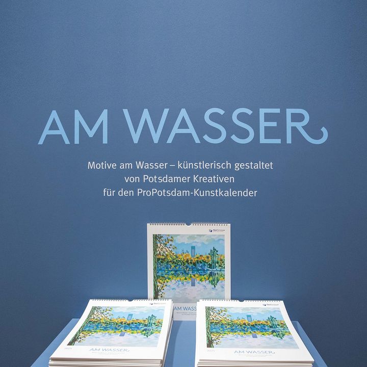 aufgestapelte Kunstkalender "Am Wasser" vor dem Ausstellungselement der Ausstellung.