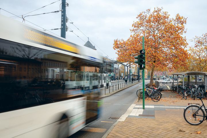 Ein Bus fährt an einer Ampel vorbei. Es sind viele Fahrradstellplätze und eine Tramhaltestelle zu sehen.